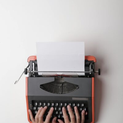 From above crop person using vintage black and red typewriter with white blank sheet of paper against white background